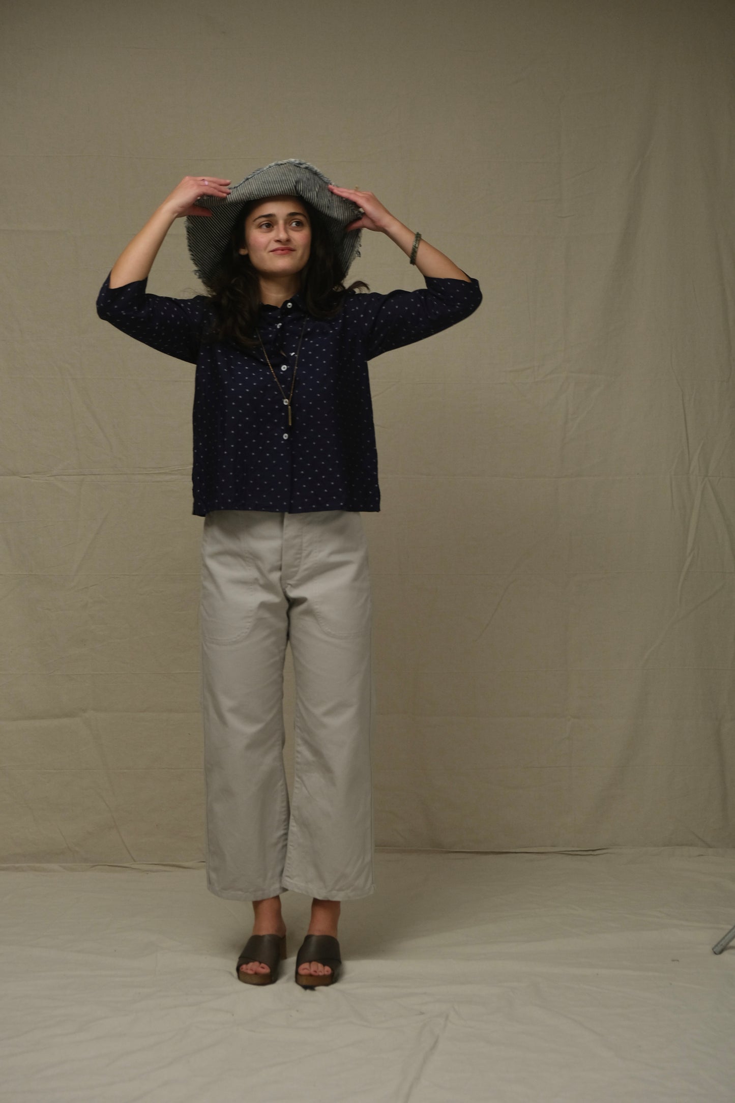 Person wearing a dark blue patterned shirt and light gray pants against a plain background