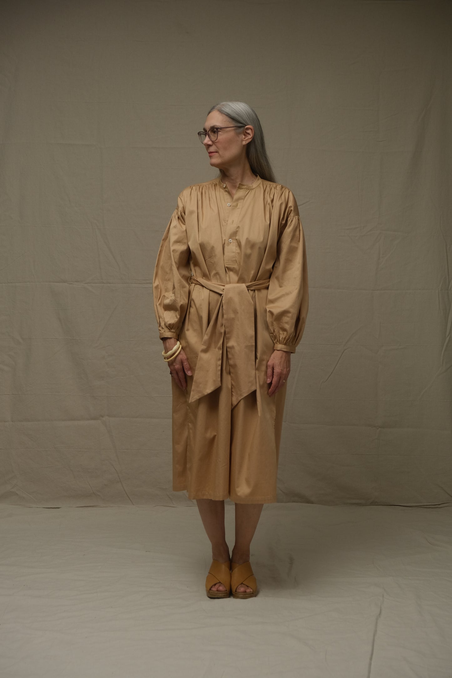 Person wearing a beige dress standing against a plain background