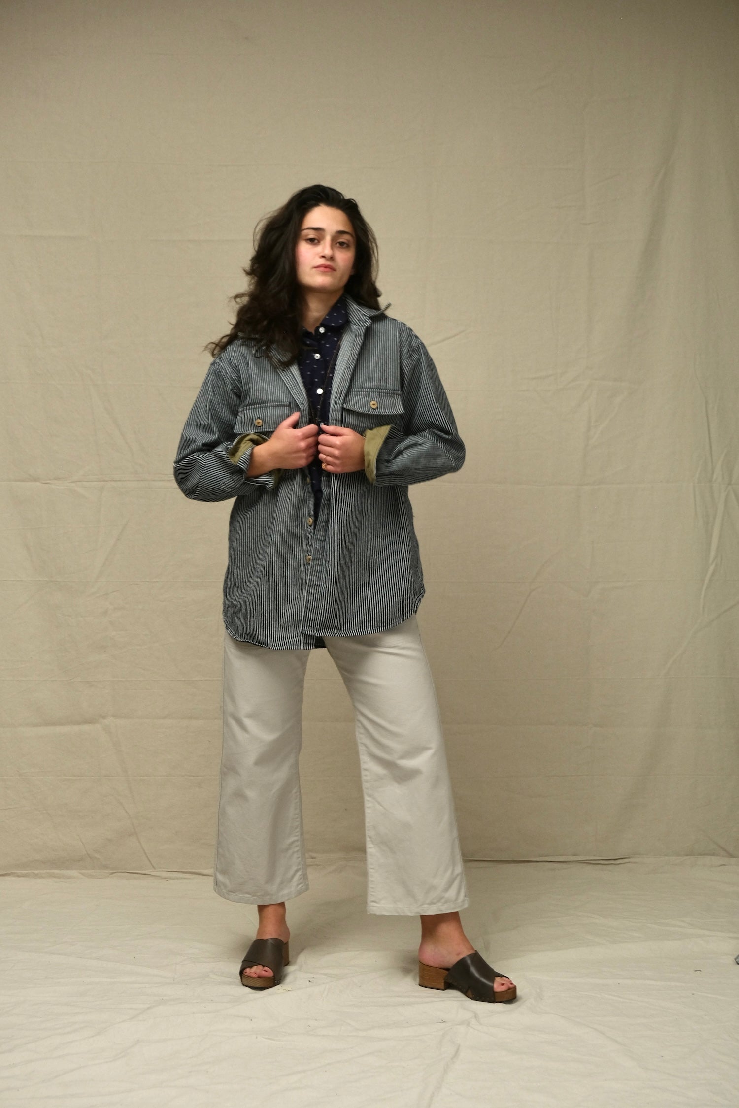 Person wearing a rr stripe jacket and white pants against a plain background