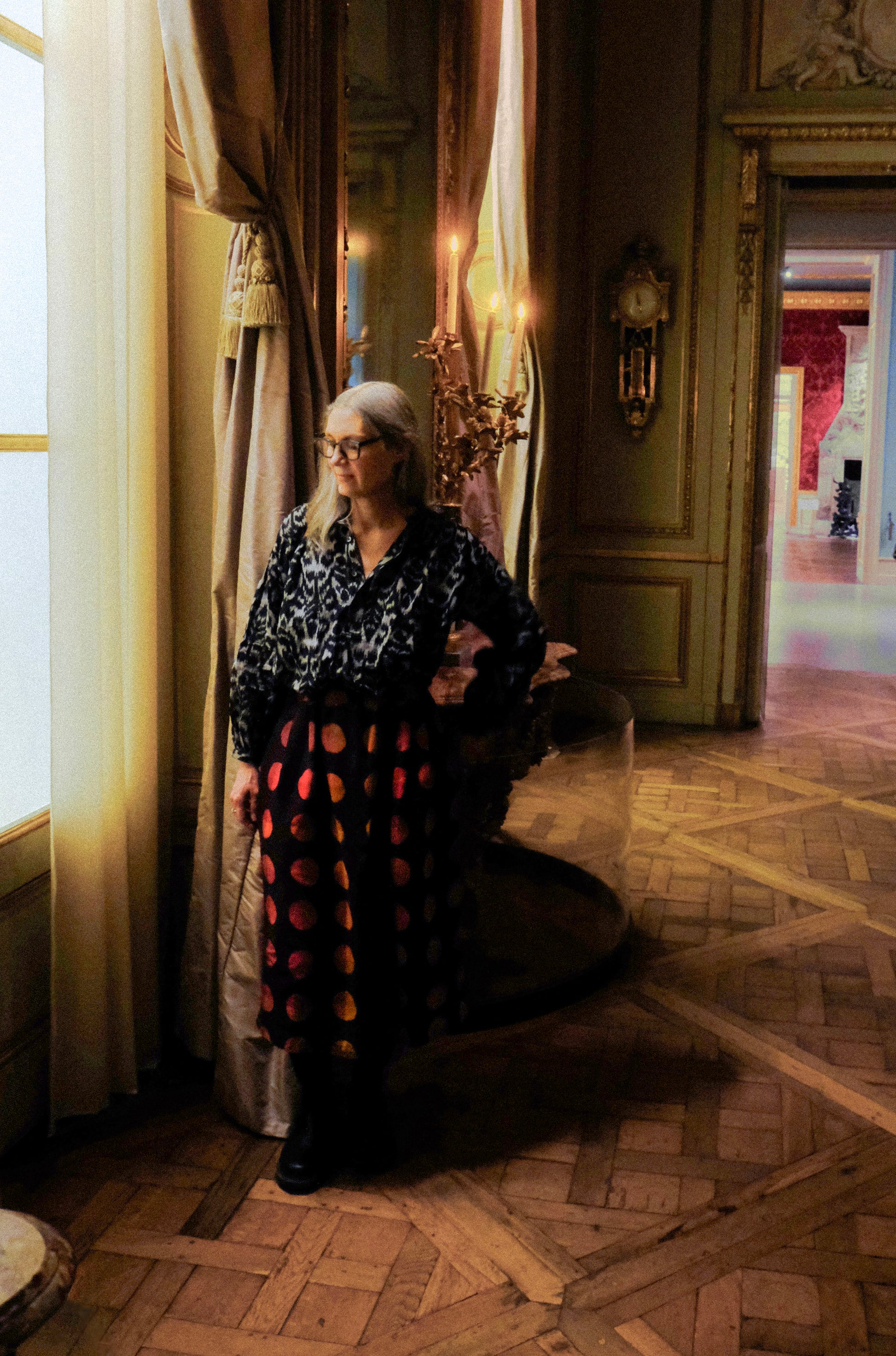 Woman wearing a black ikat peasant blouse standing in an elegant room with ornate decor