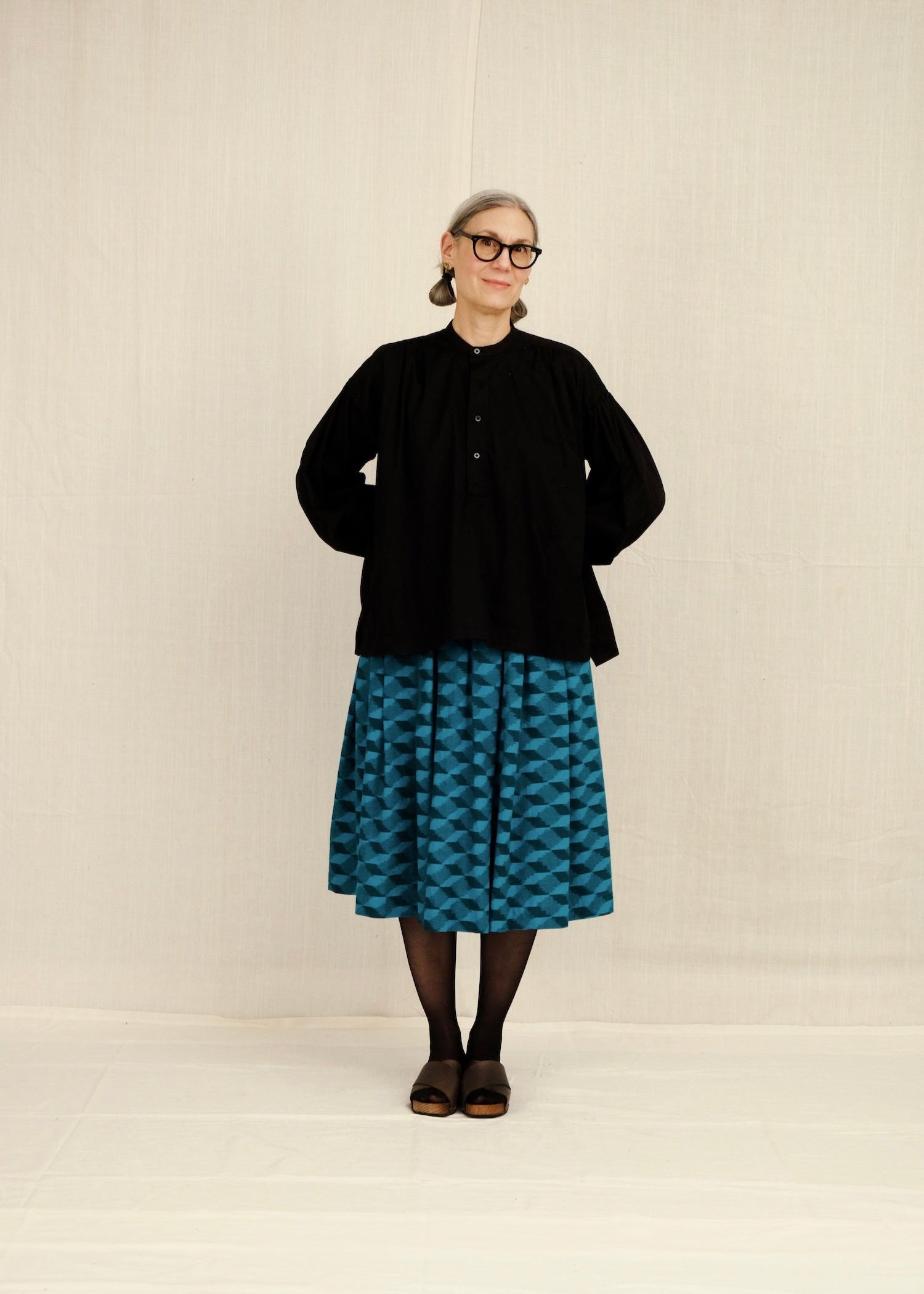 Person wearing a black PEASANT BLOUSE and blue patterned BELLE skirt on a plain background