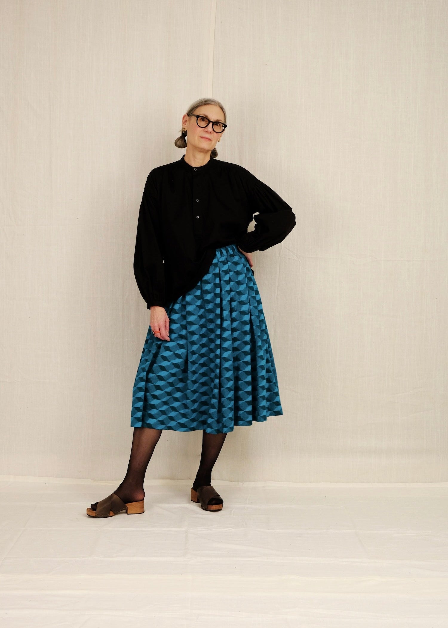 Person wearing a black peasant blouse and blue patterned skirt on a plain background