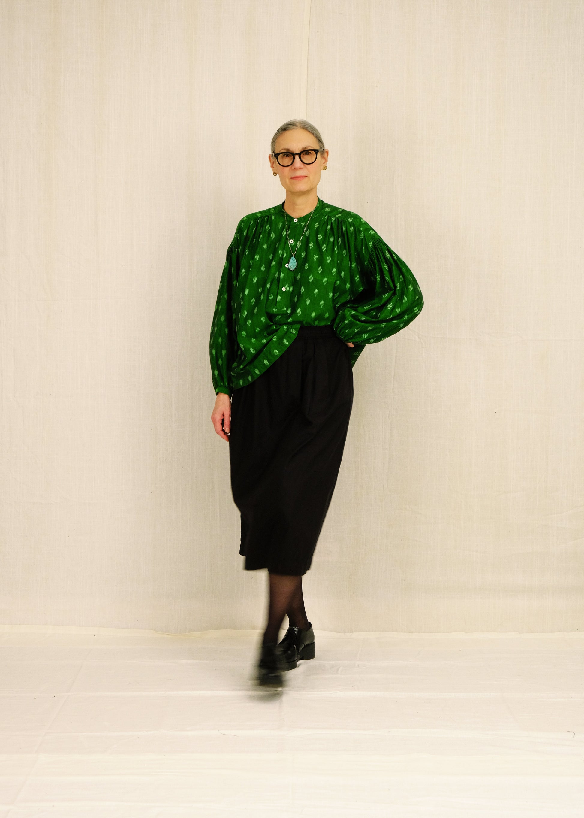 Person wearing a green patterned top and black skirt on a plain background