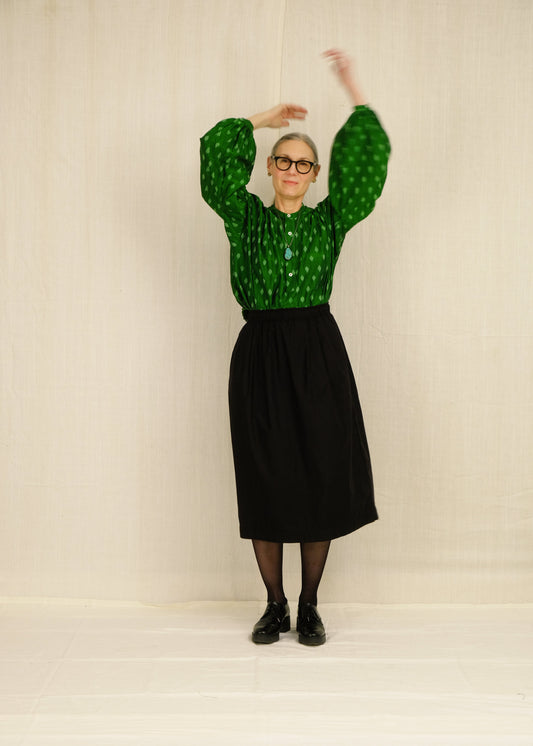 Person wearing a green patterned peasant blouse and black demi-belle skirt against a plain background
