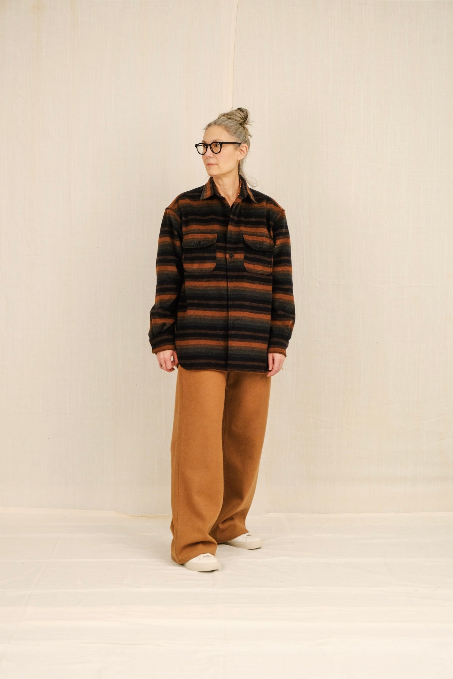 Person wearing a striped overshirt and camel long sailor pants against a plain background