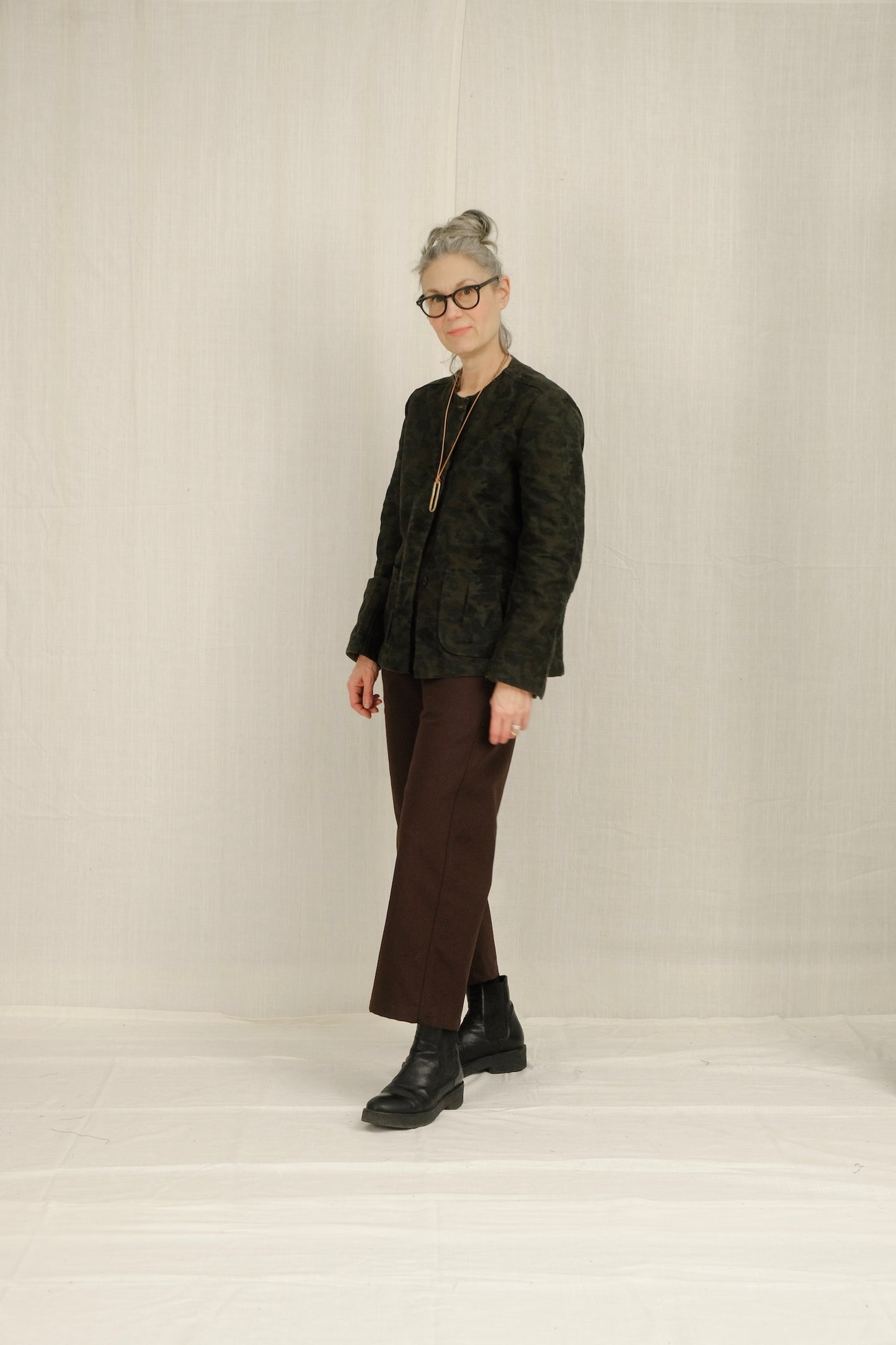 Person wearing a dark patterned blazer, brown SAILOR pants, and black shoes on a plain background