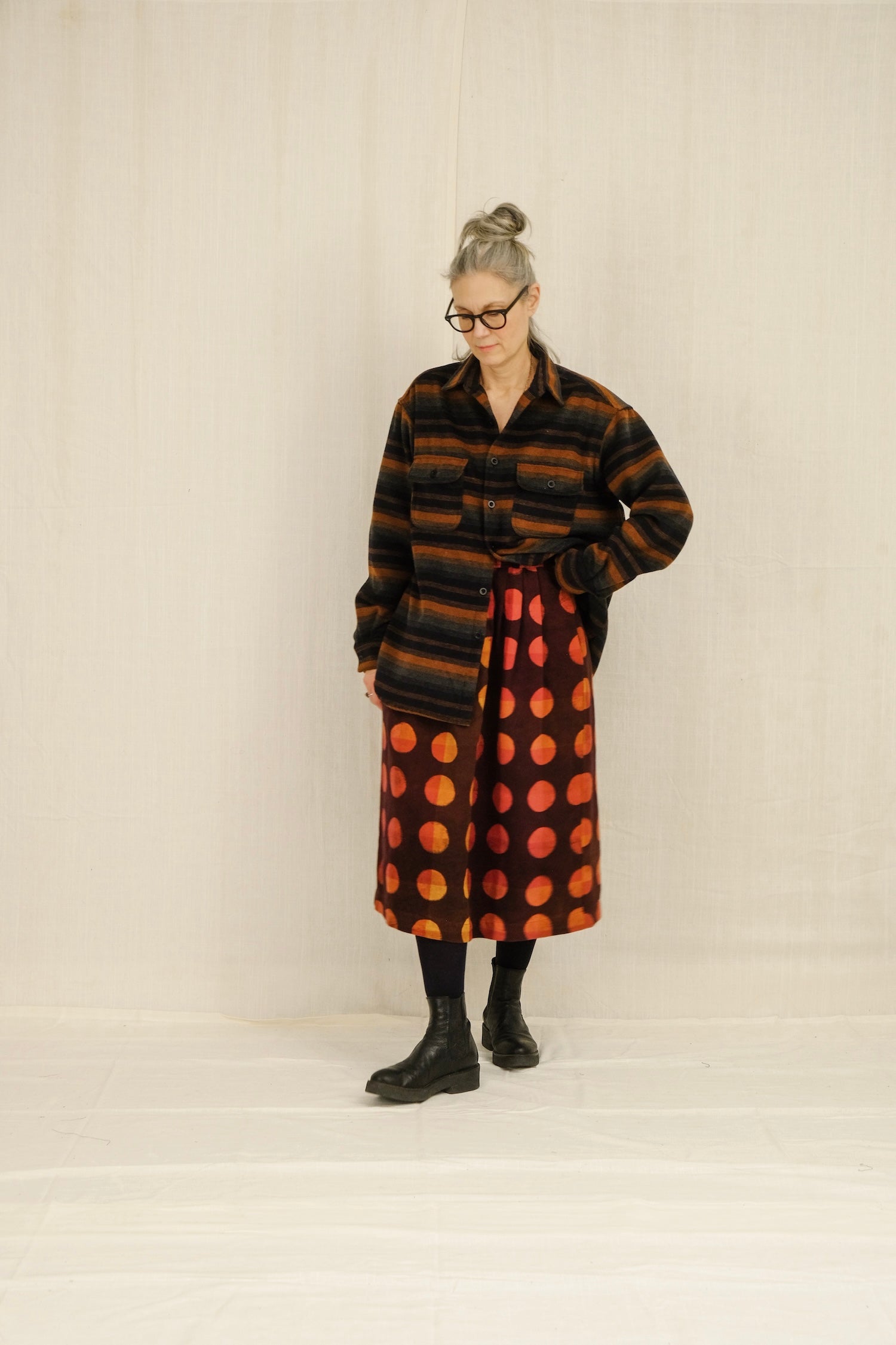 Person wearing a long, multi-striped patterned overshirt with a plain background