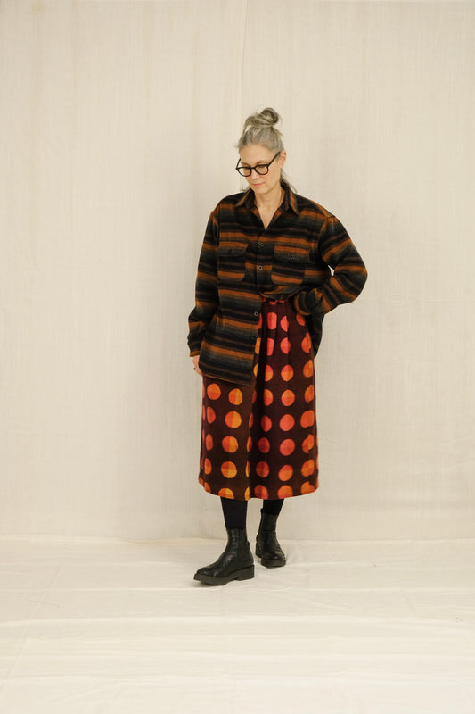 Person wearing a long, multi-striped patterned overshirt with a plain background