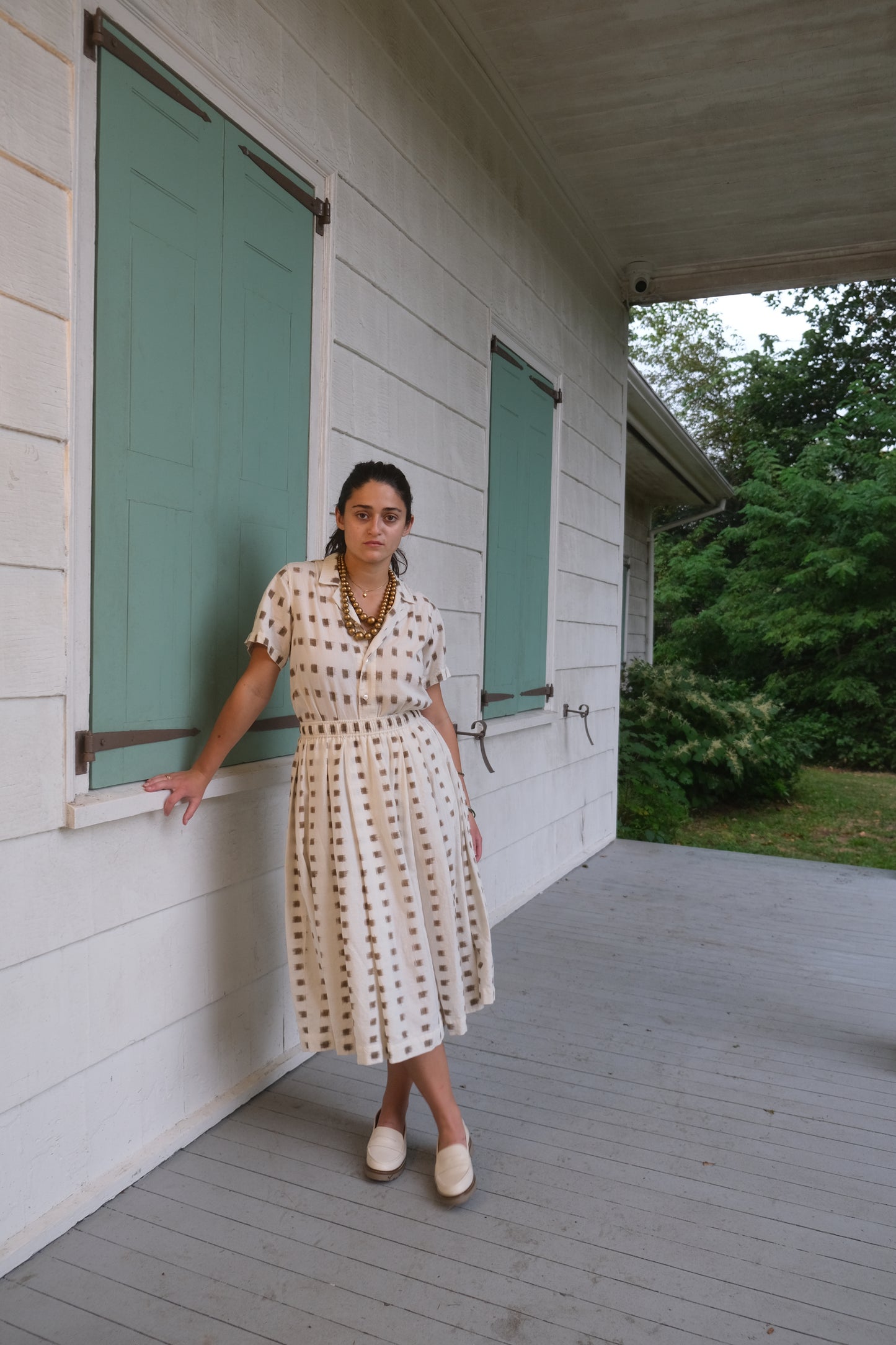 Woman standing in a doorway with green shutters and a wooden wall.
