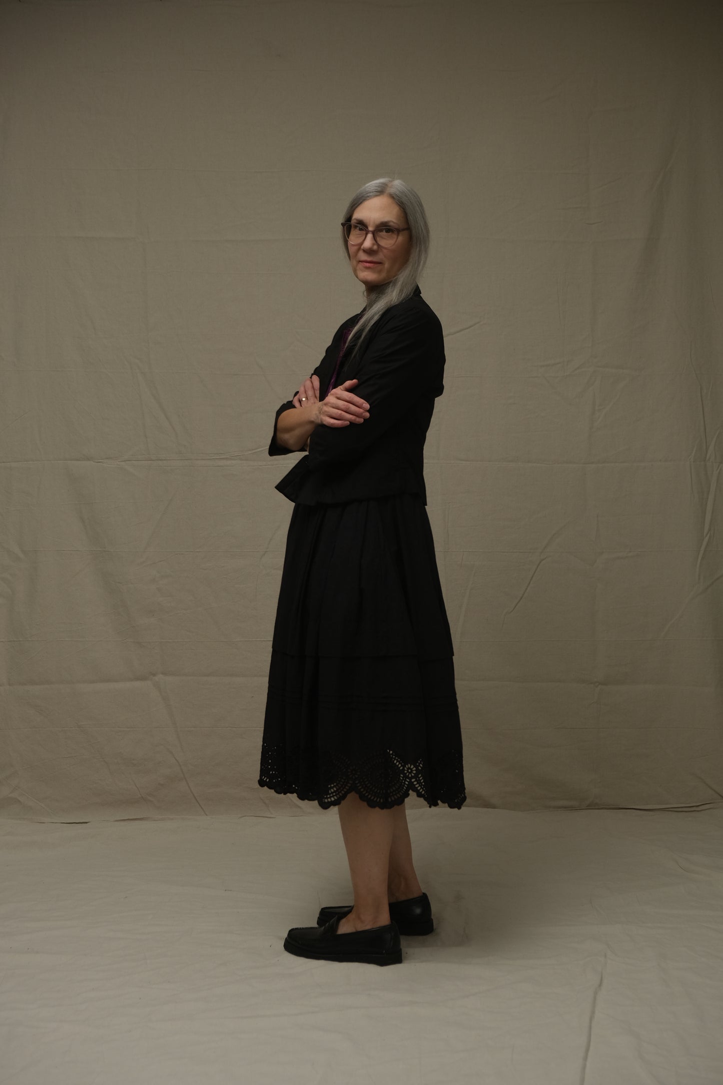 Person wearing a black jacket and skirt standing on a plain background