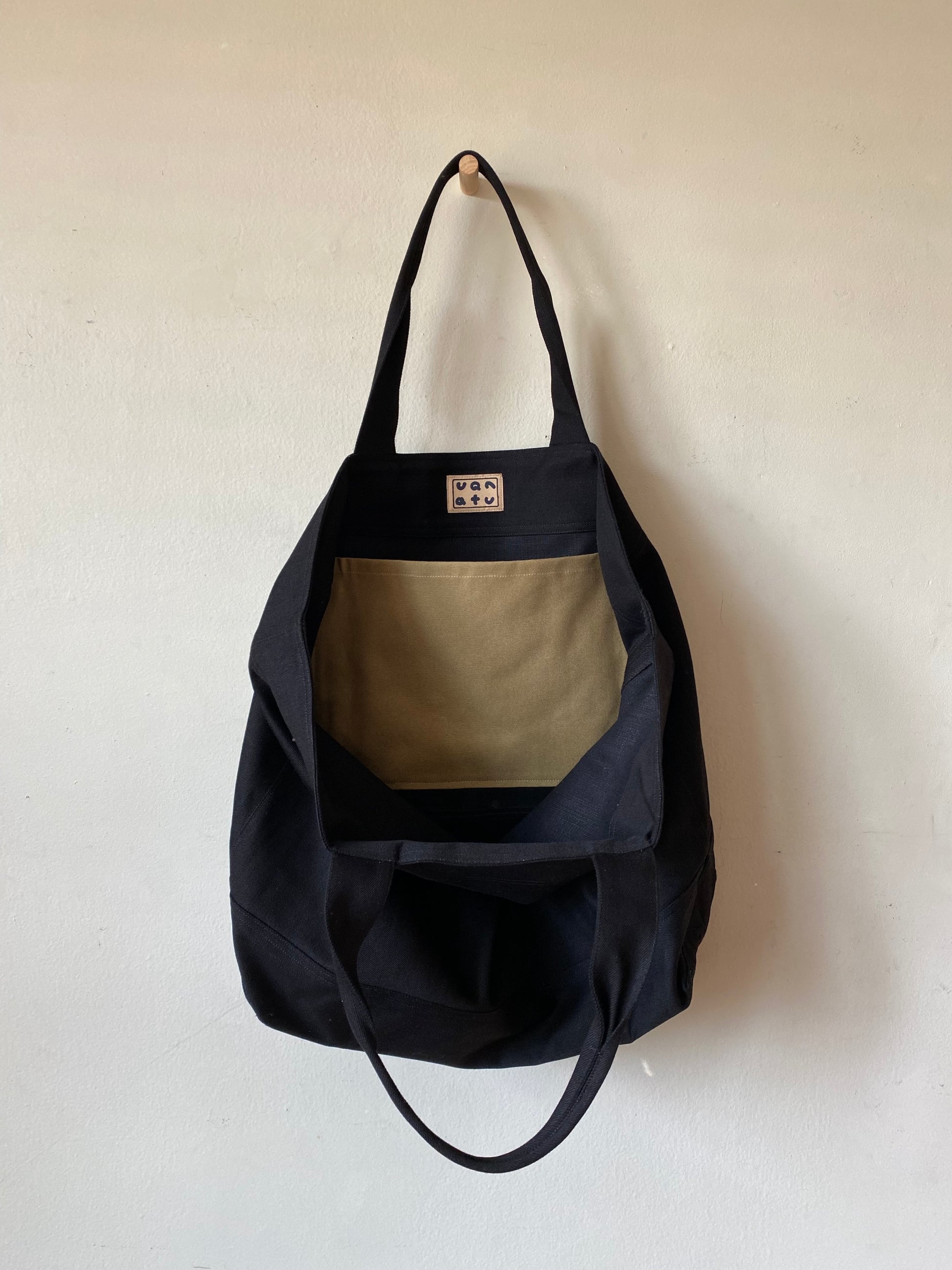 Black tote bag with beige pocket on a white background