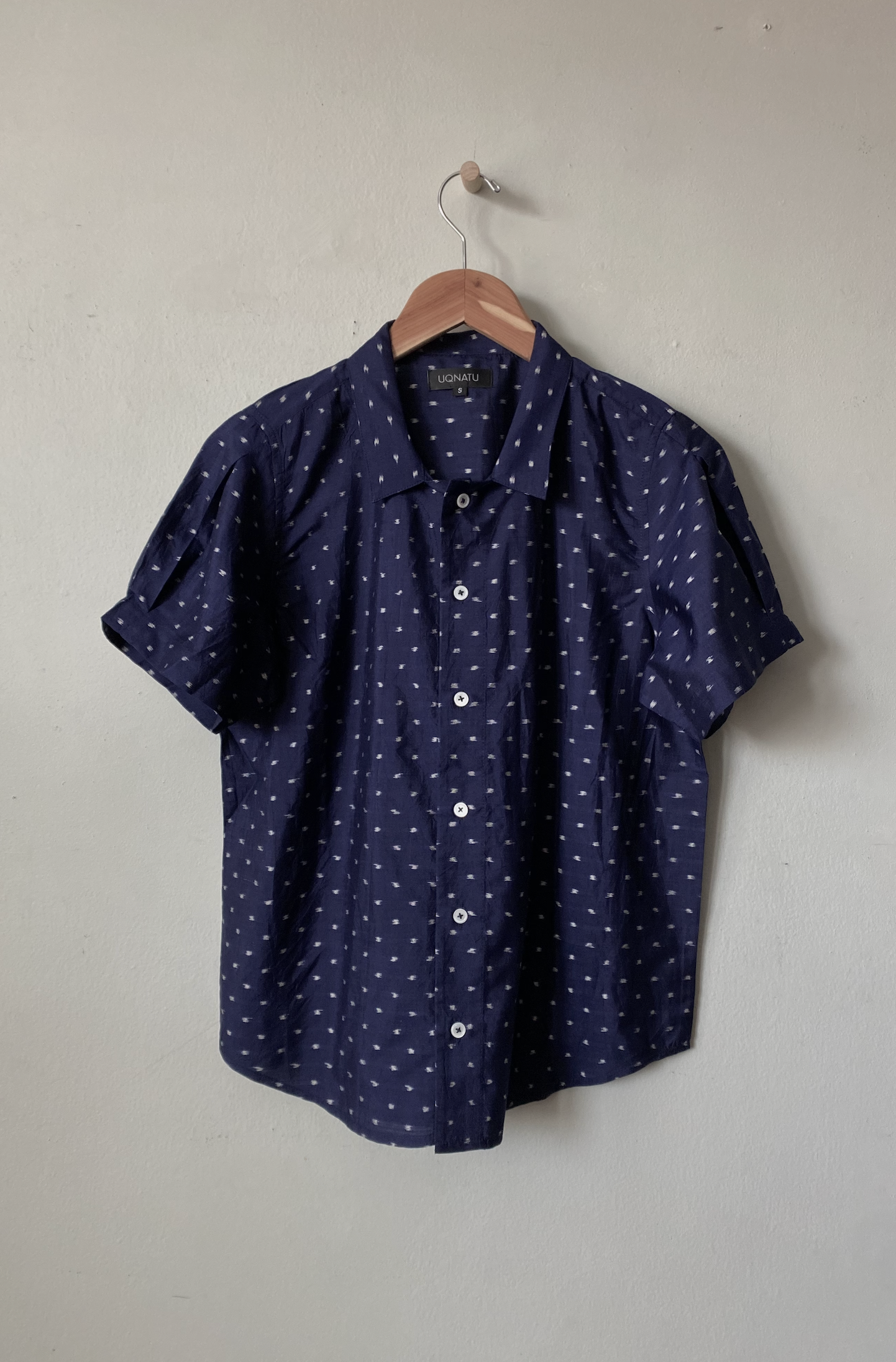 Navy blue shirt with white pattern on a hanger against a plain wall