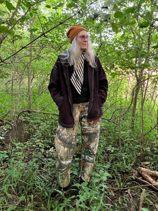 Person in camouflage pants and a dark jacket standing in a forest