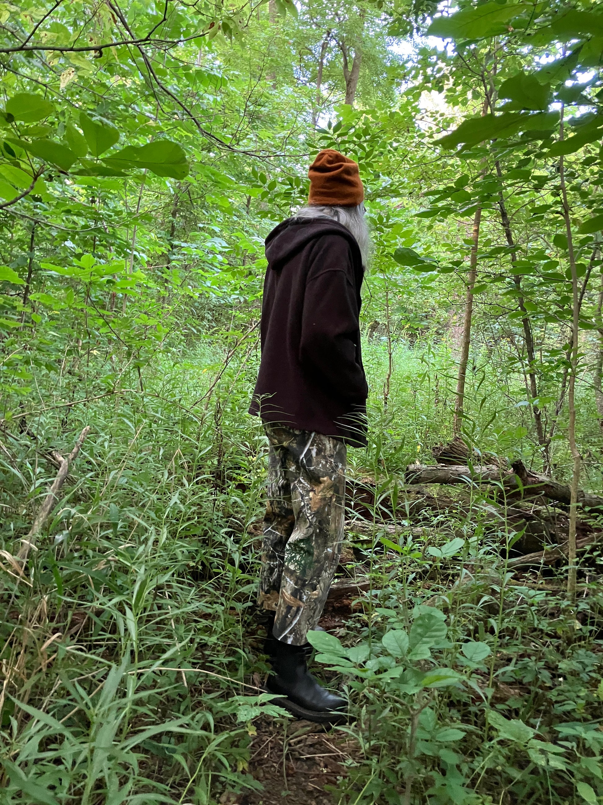 Person in camouflage pants and a brown jacket walking through a forest