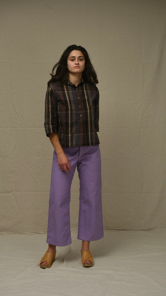 Person wearing a plaid shirt and purple pants standing against a plain background
