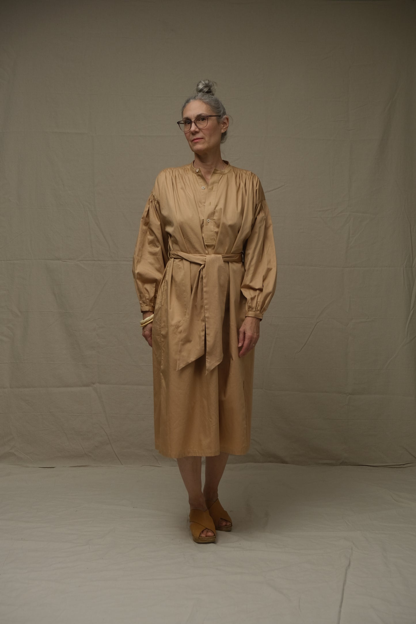 Person wearing a beige dress standing against a plain background