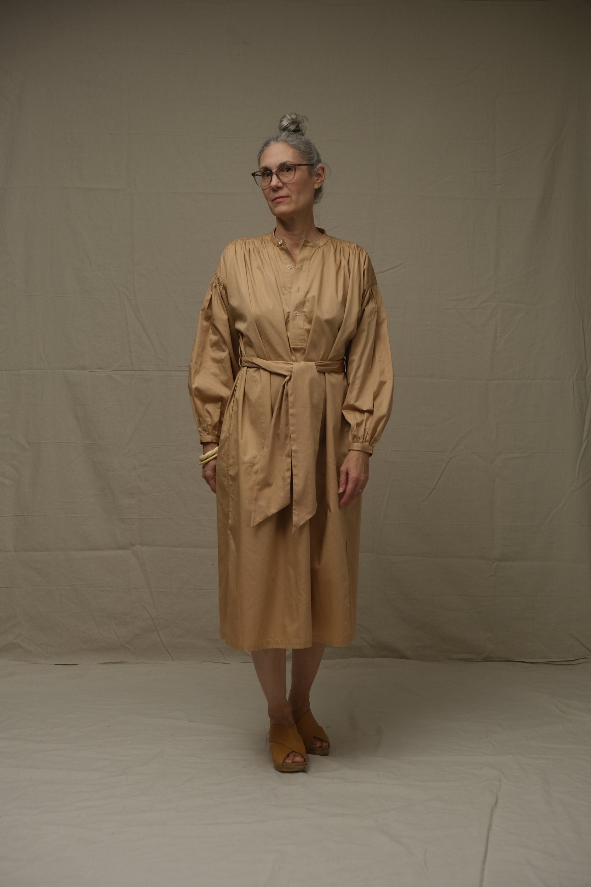 Person wearing a beige dress standing against a plain background