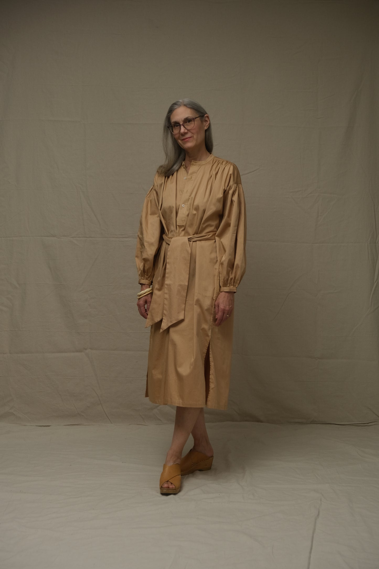 Person wearing a beige dress standing on a plain background