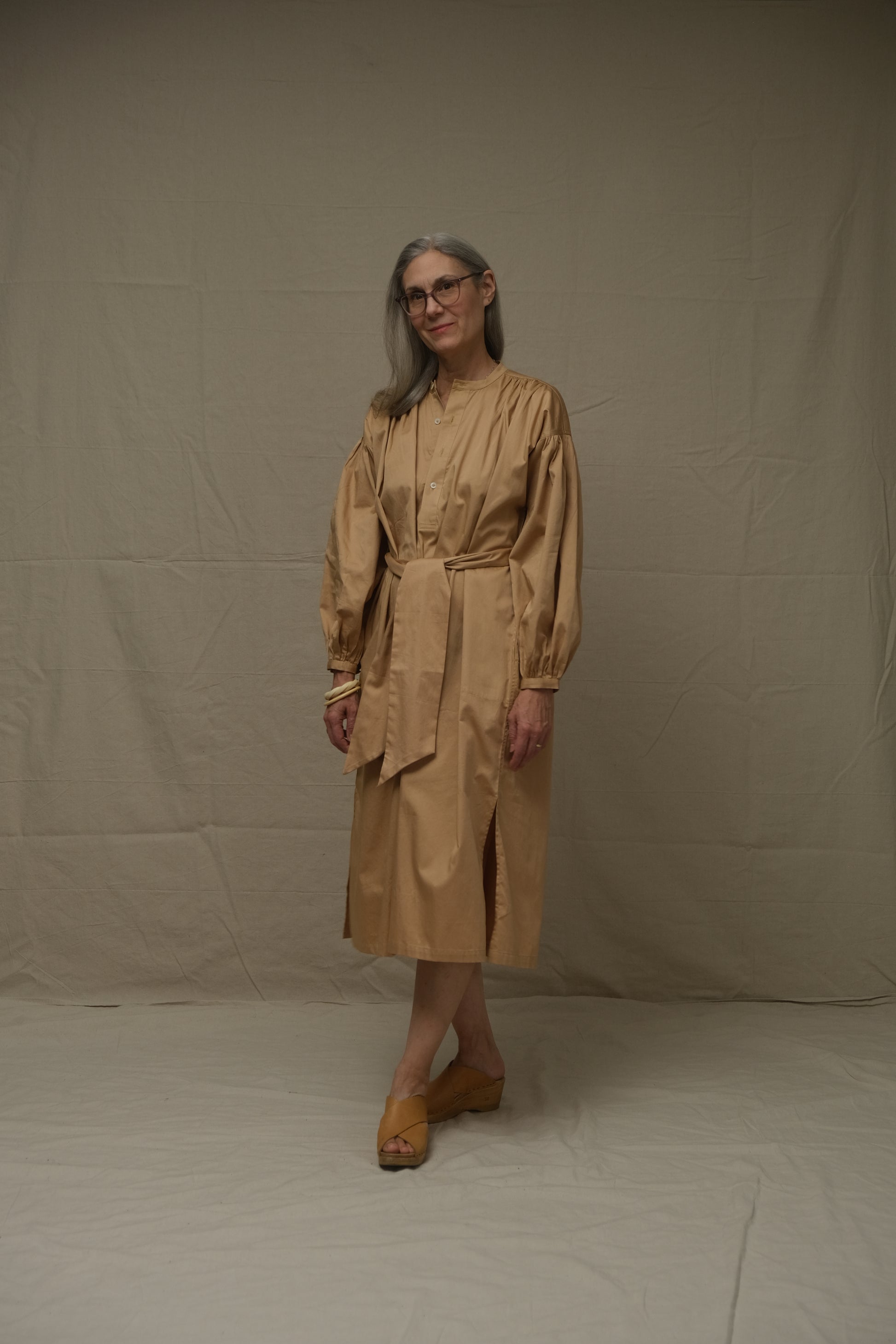 Person wearing a beige dress standing on a plain background