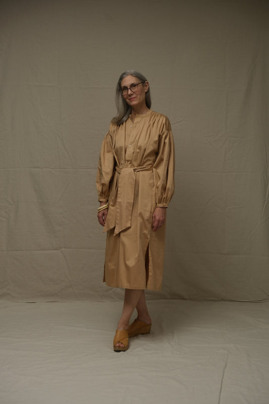 Person wearing a beige dress standing on a plain background