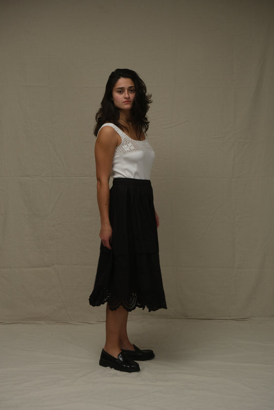 Woman in a black skirt and white top standing against a plain background