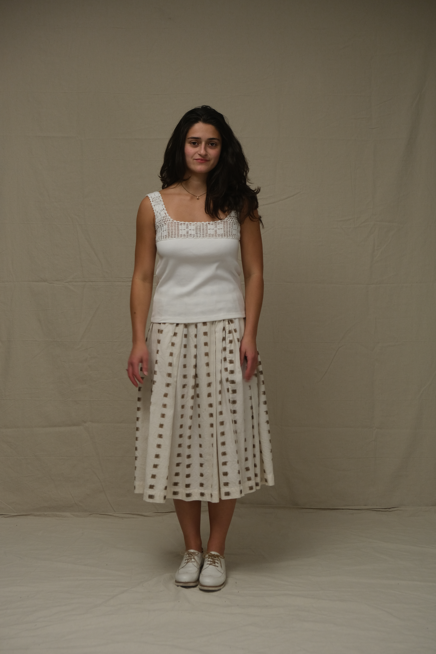 Woman wearing a white sleeveless top and patterned skirt against a plain background