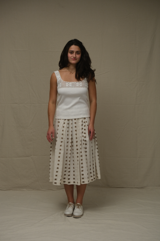 Woman wearing a white sleeveless top and patterned skirt against a plain background