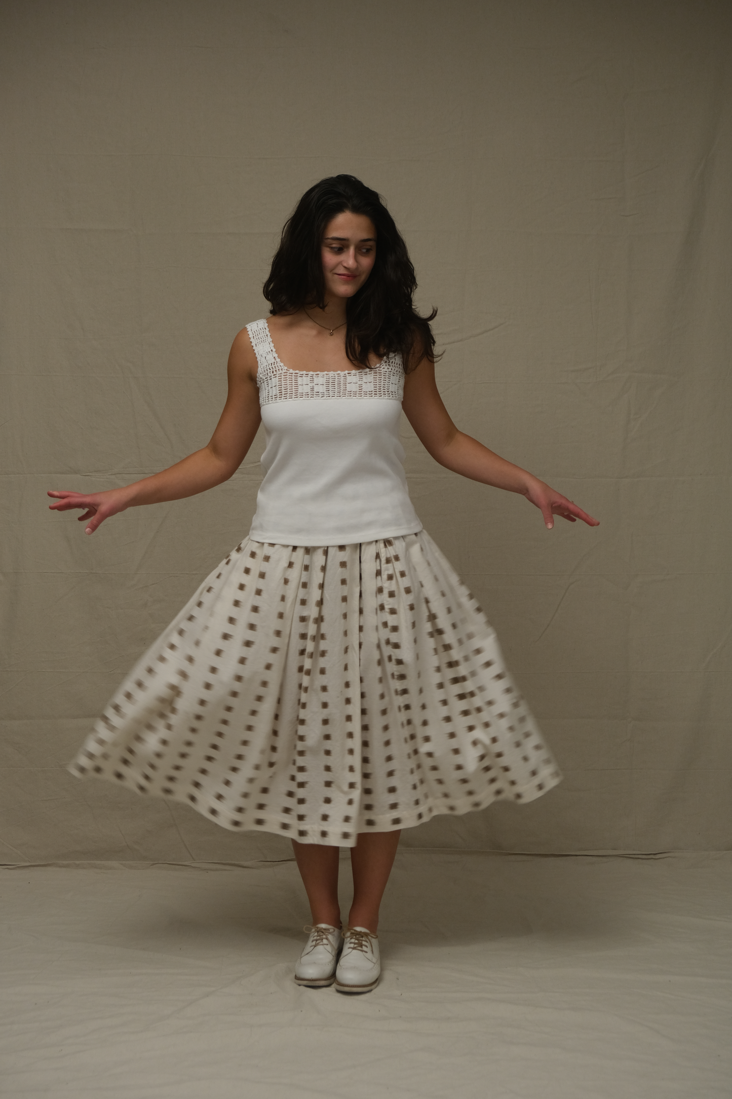 Woman wearing a white top and polka dot skirt against a plain background