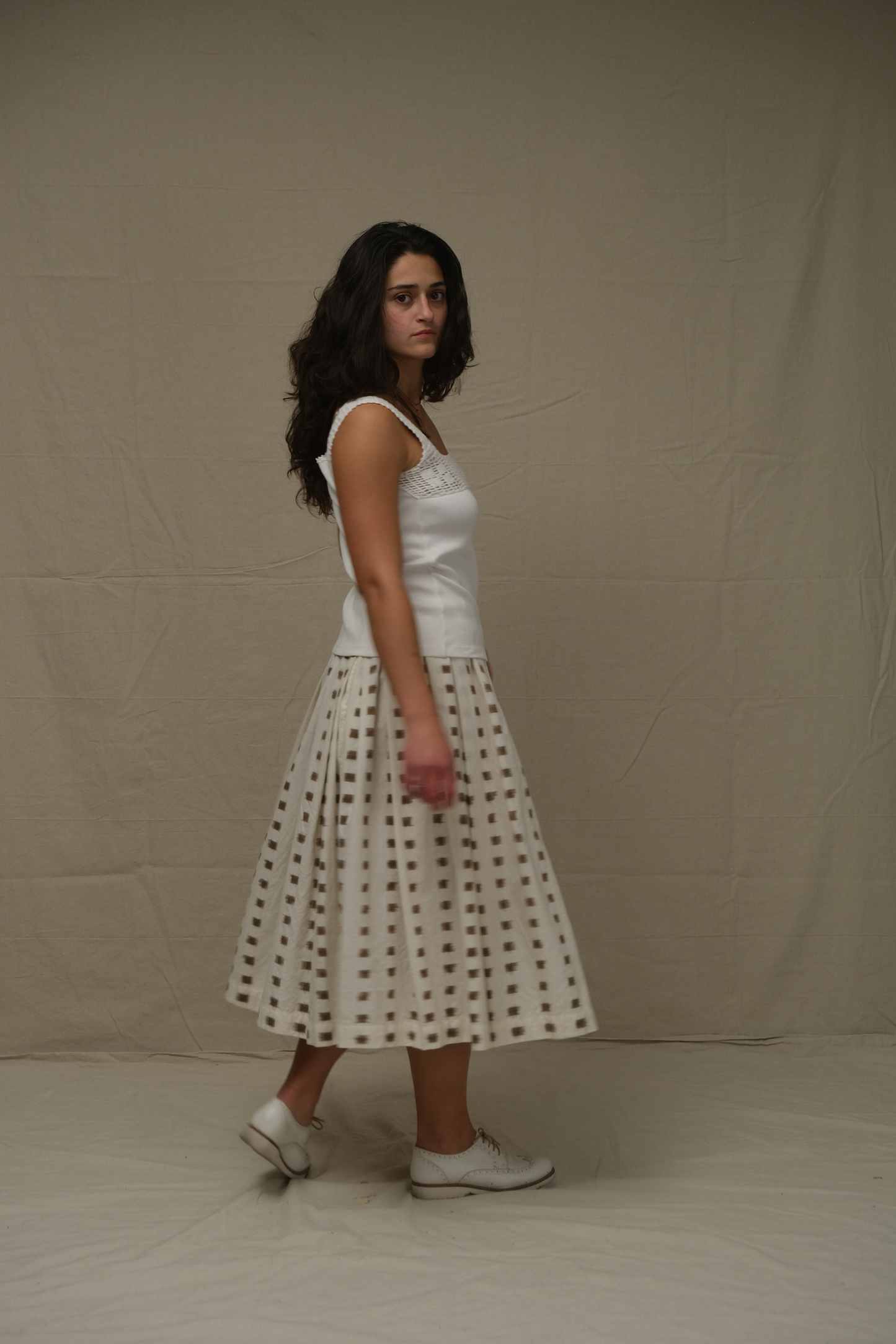 Woman wearing a white sleeveless top and polka dot skirt against a plain background