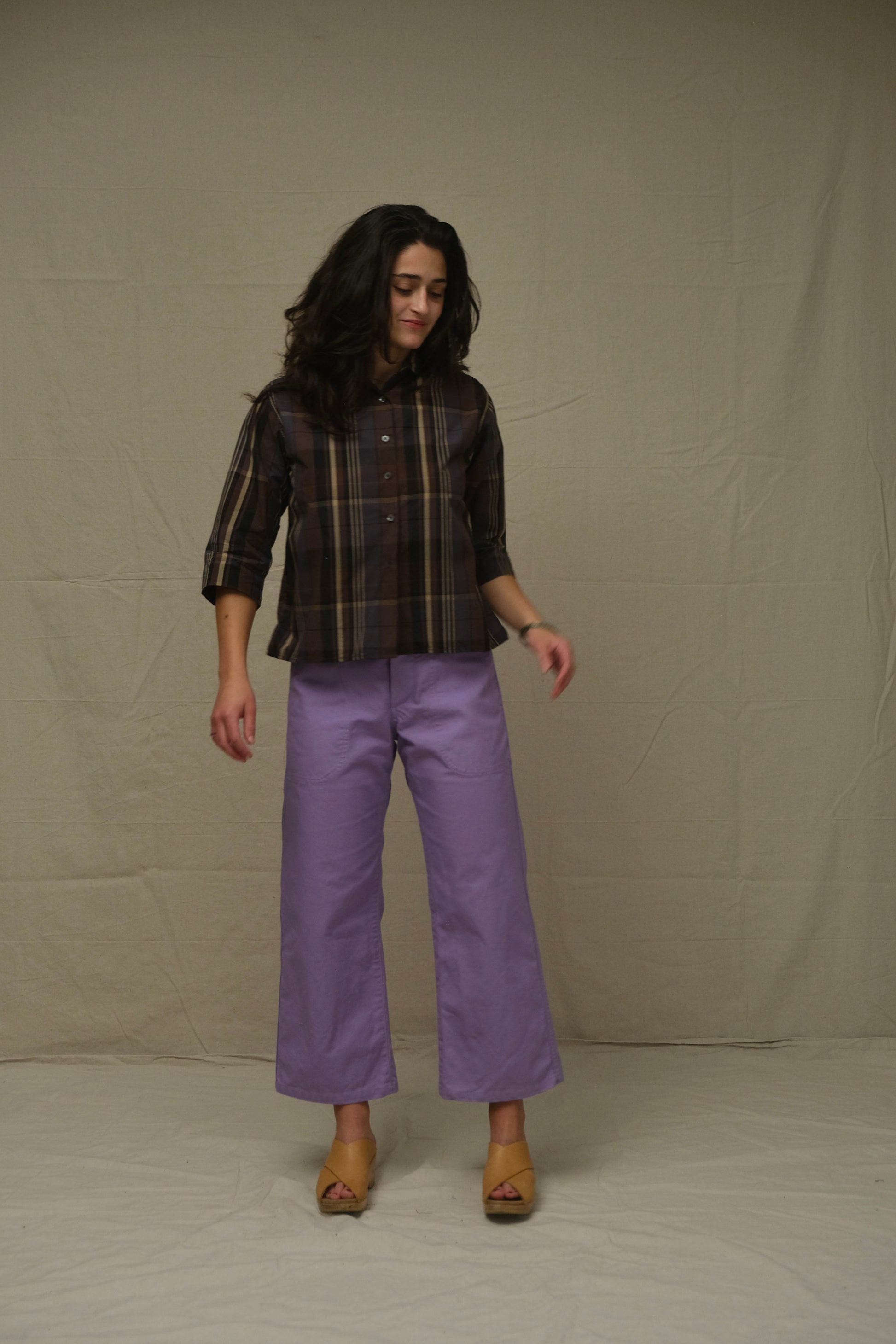 Woman wearing a plaid shirt and purple pants against a plain background