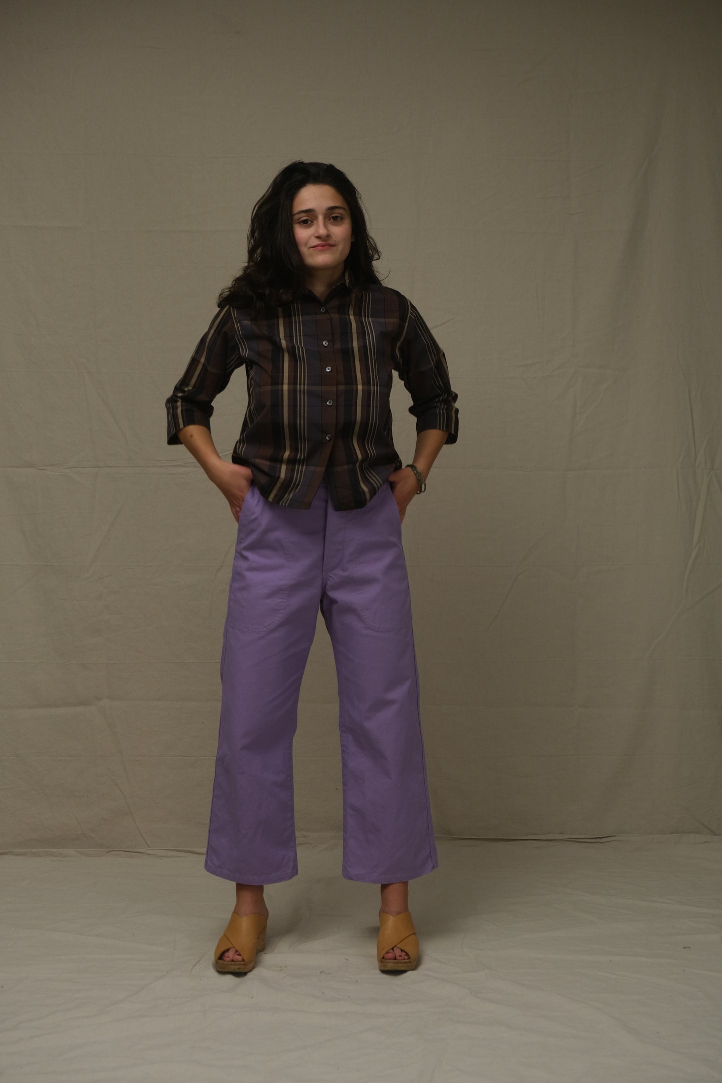 Person wearing a plaid shirt and purple pants on a plain background