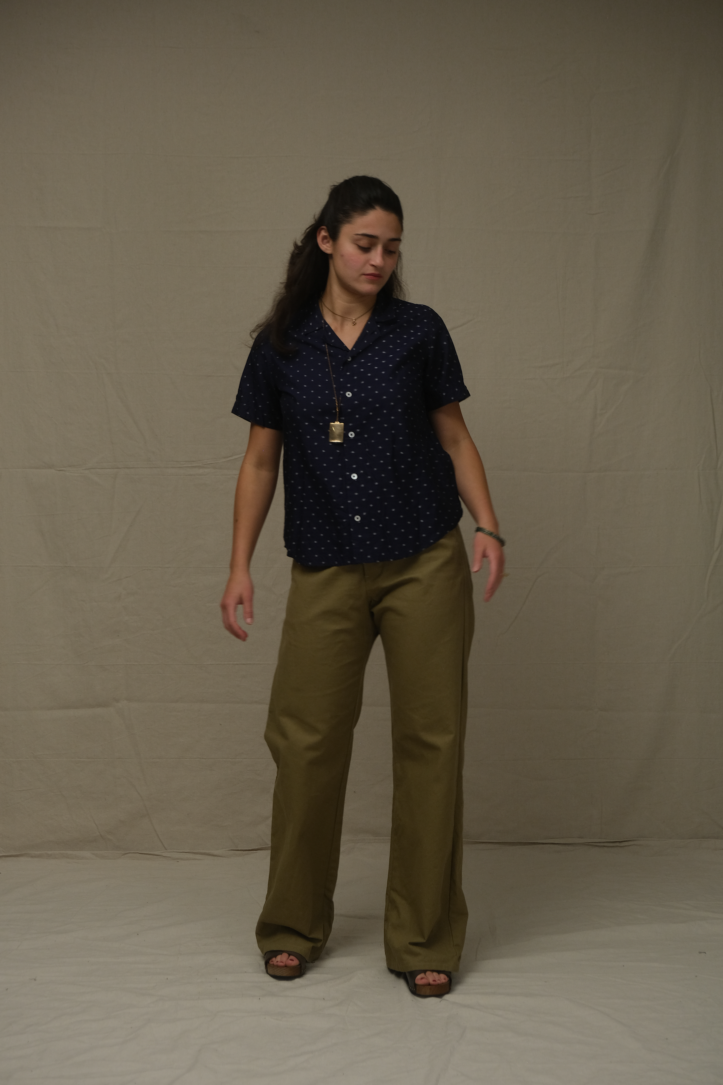 Woman wearing a dark blue patterned shirt and beige pants against a plain background