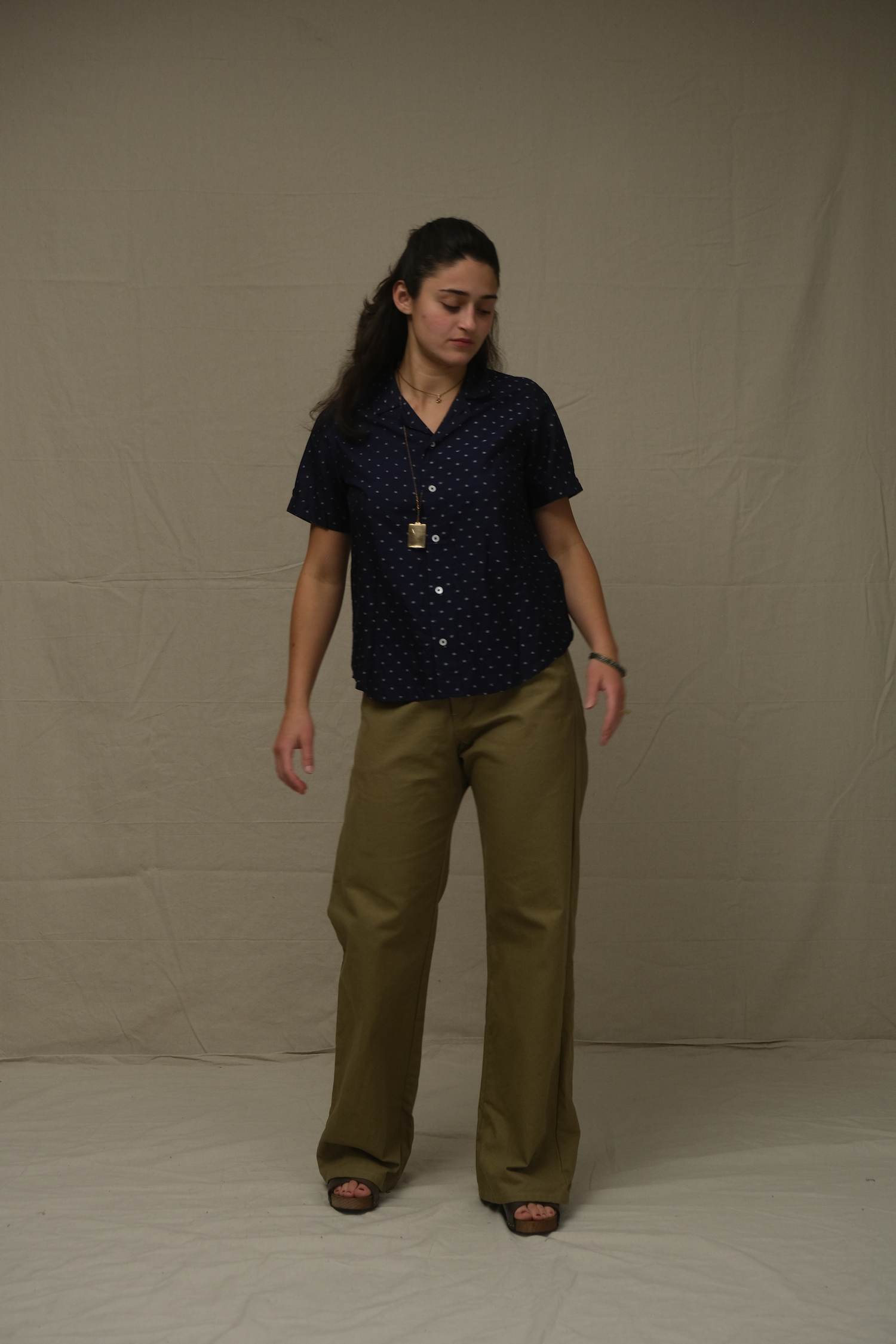 Woman wearing a dark blue patterned shirt and beige pants against a plain background