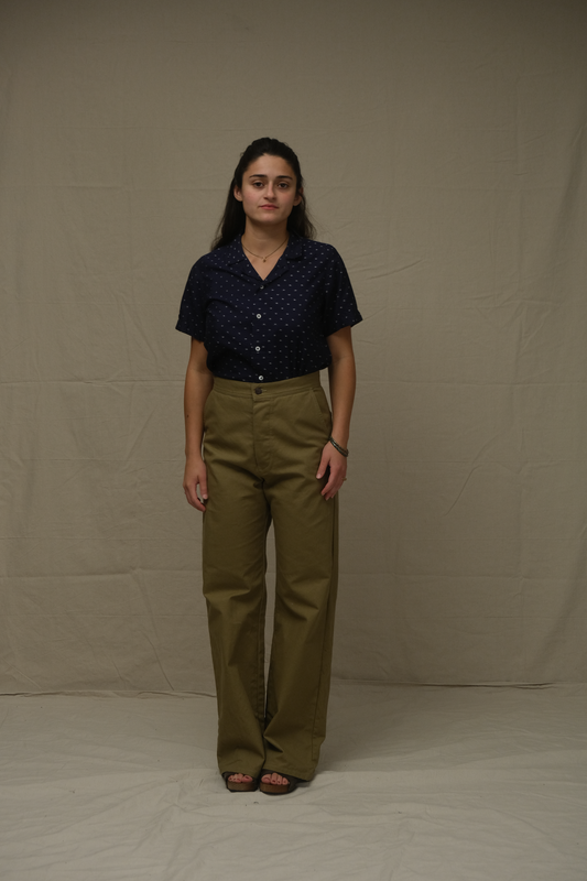 Person wearing a dark blue shirt and olive green pants against a beige background