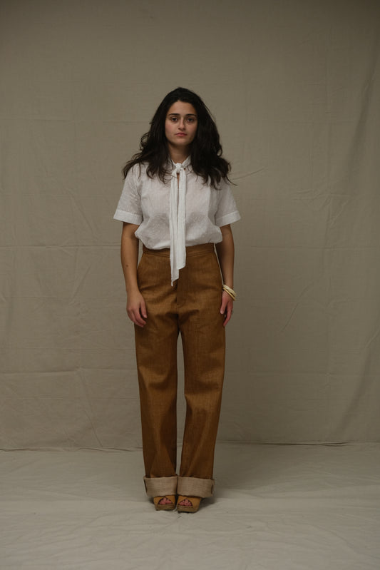 Woman wearing a white blouse and brown pants standing on a plain background
