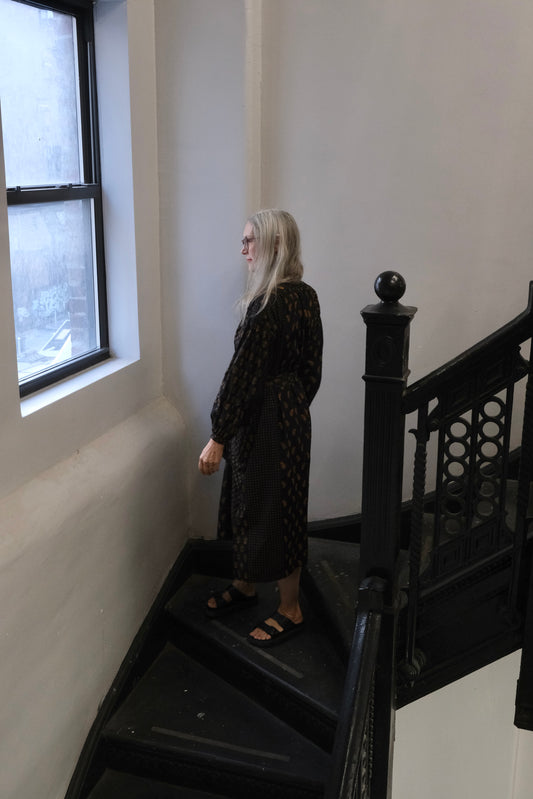 Person in a black dress standing on a staircase next to a window