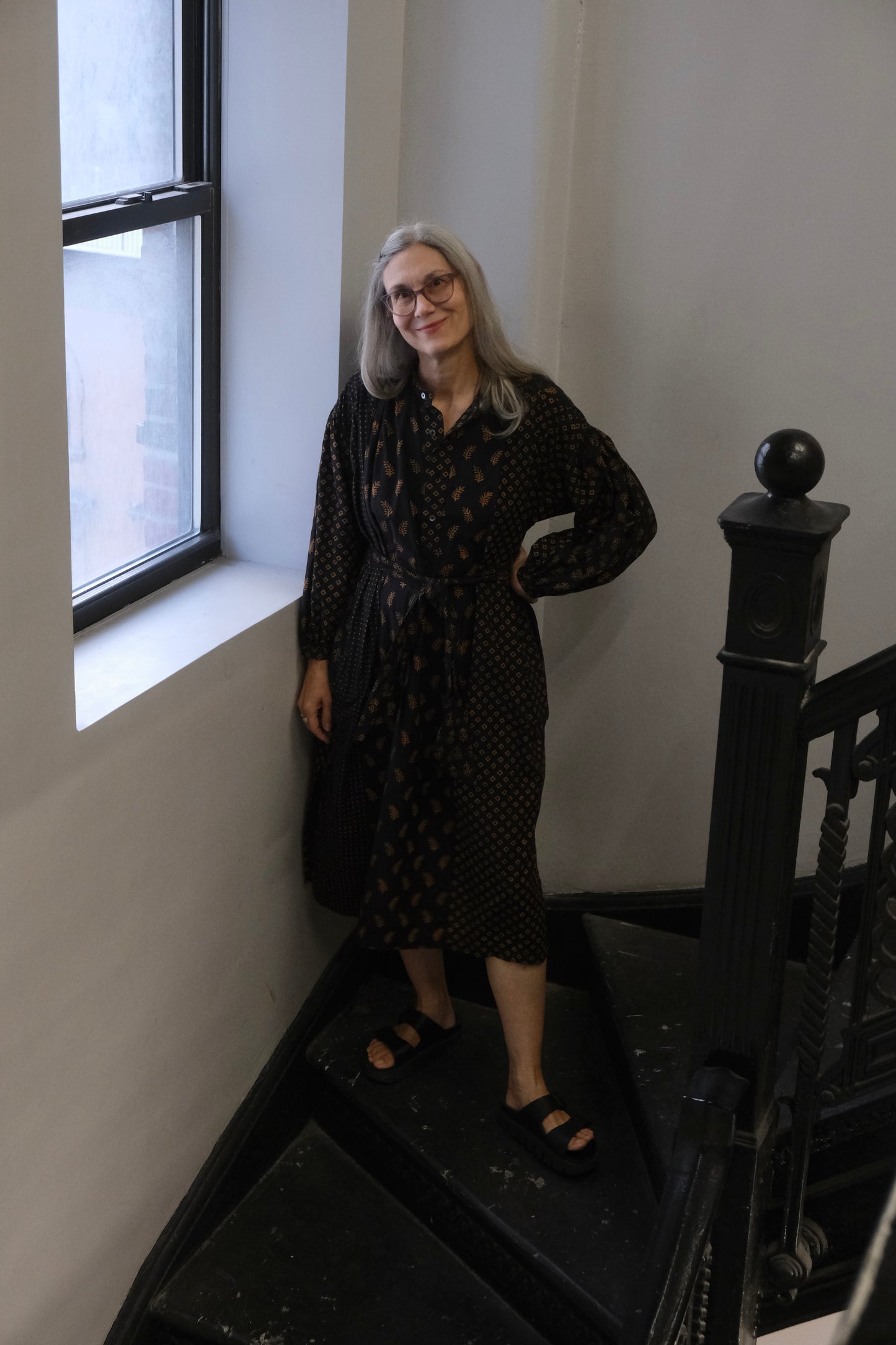 Woman standing on a staircase next to a window in a room with white walls.