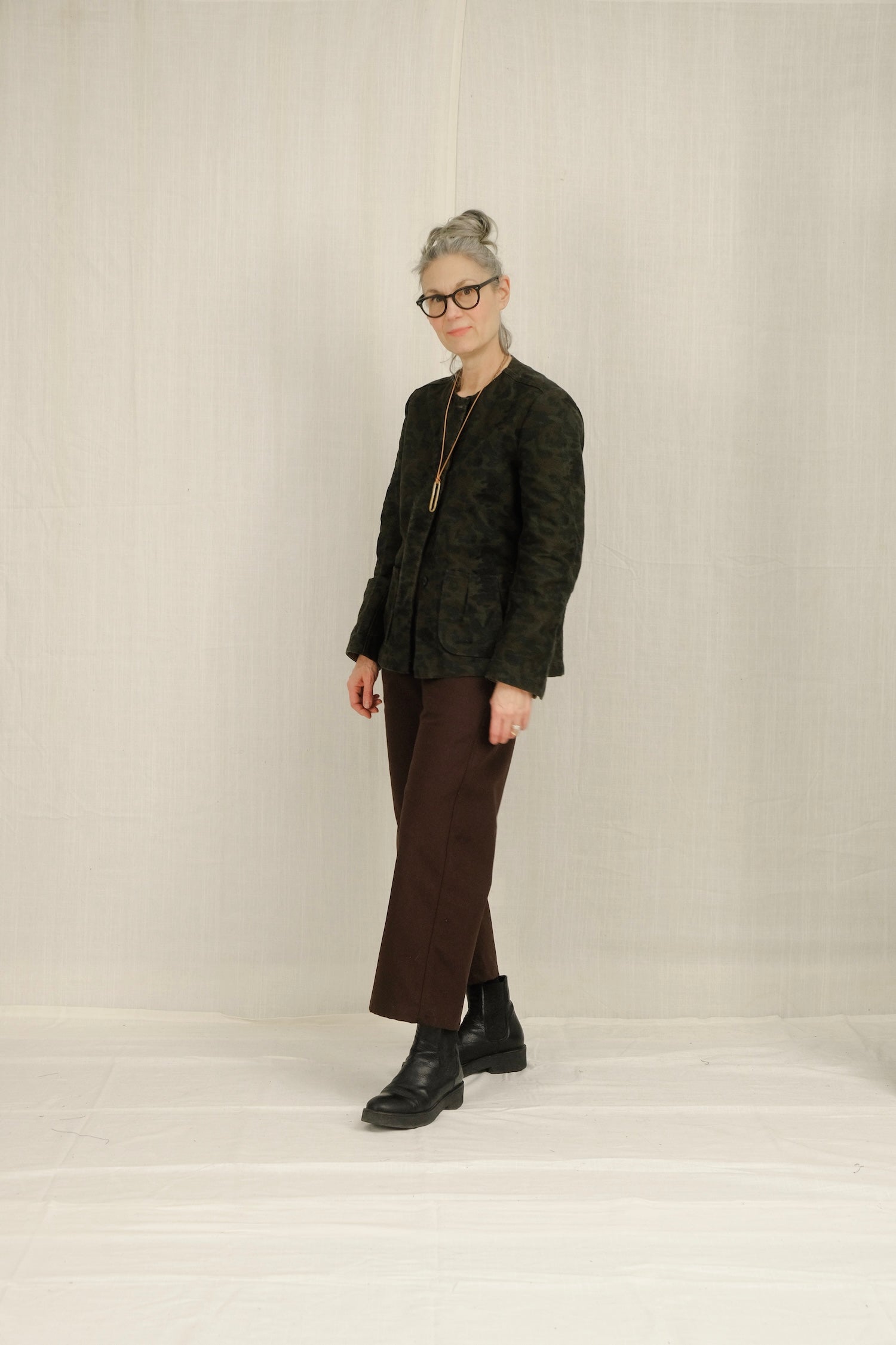 Person wearing a dark patterned blazer, brown SAILOR pants, and black shoes on a plain background