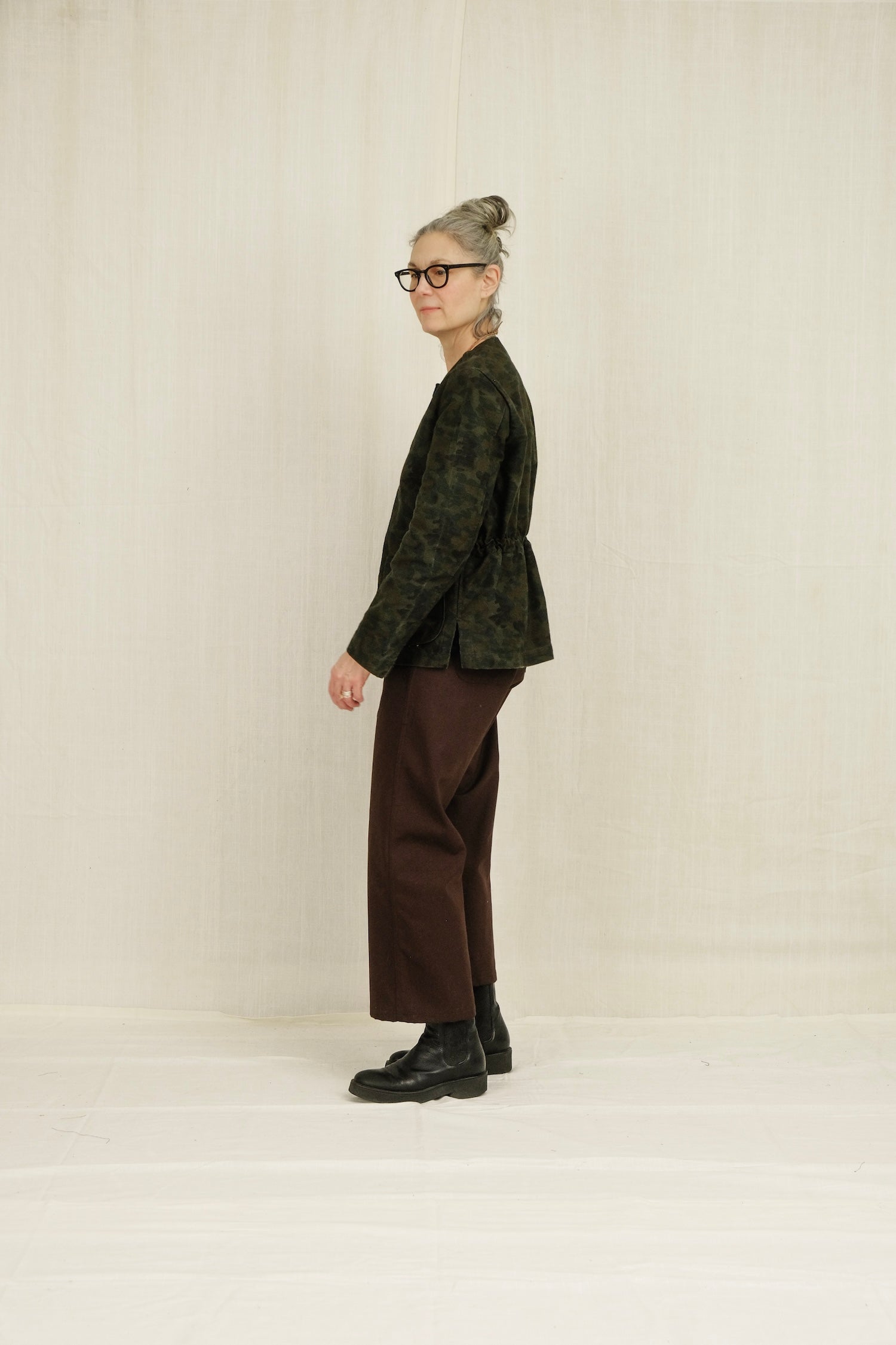 Person wearing a green patterned jacket and brown SAILOR pants standing against a plain background