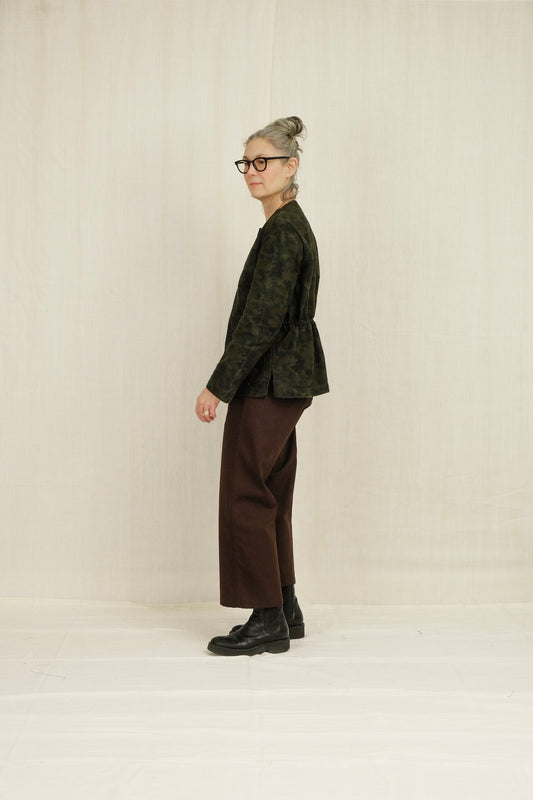 Person wearing a green patterned jacket and brown SAILOR pants standing against a plain background