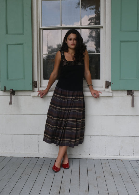 Woman standing on a wooden porch with green shutters and white walls.