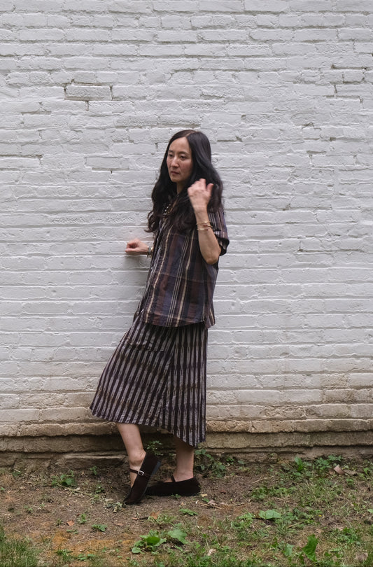 Woman standing against a white brick wall wearing a patterned dress.