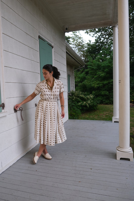 Woman in a patterned dress standing on a porch with a green doormat.