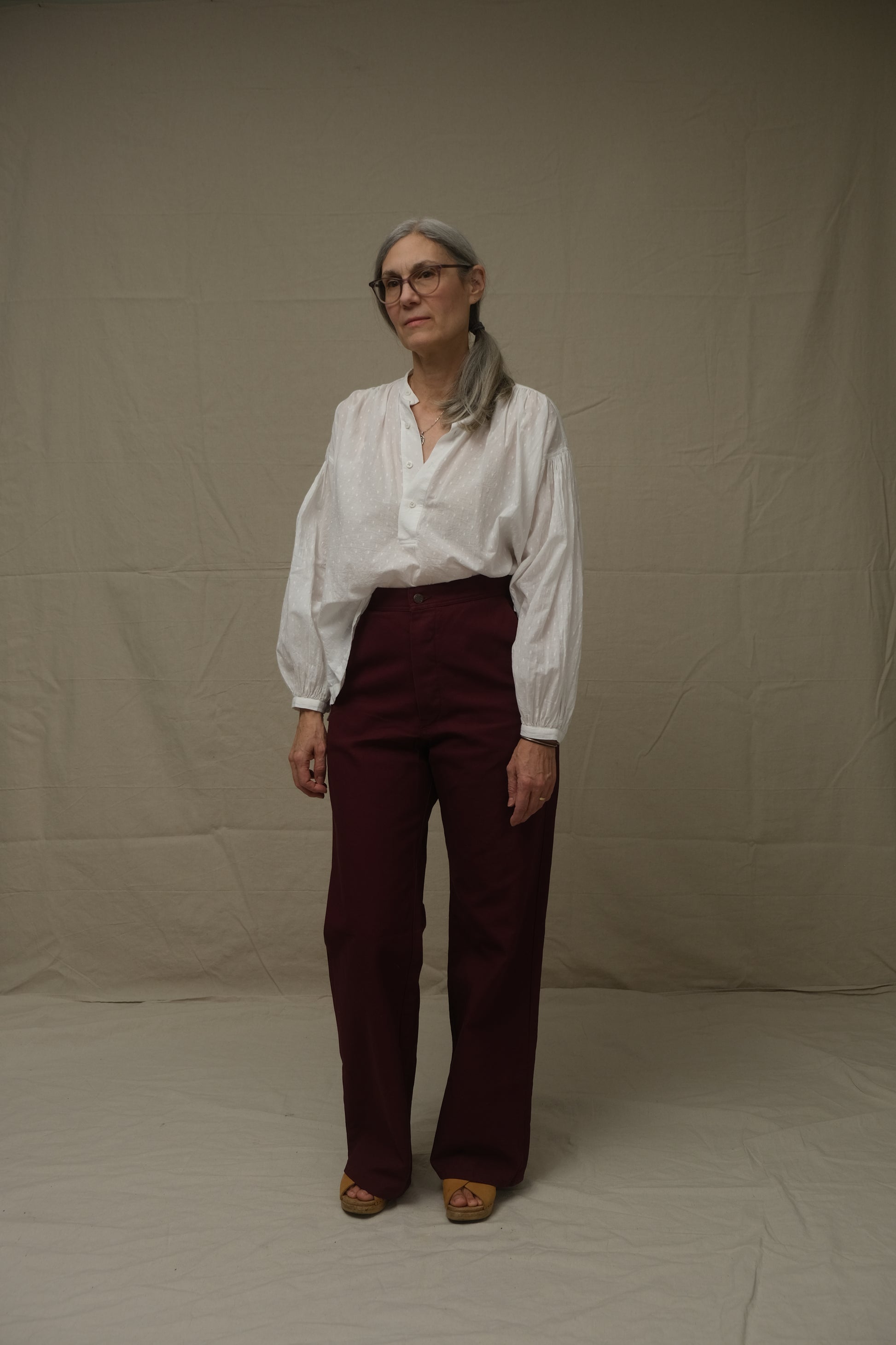 Person wearing a white shirt and maroon pants standing on a plain background