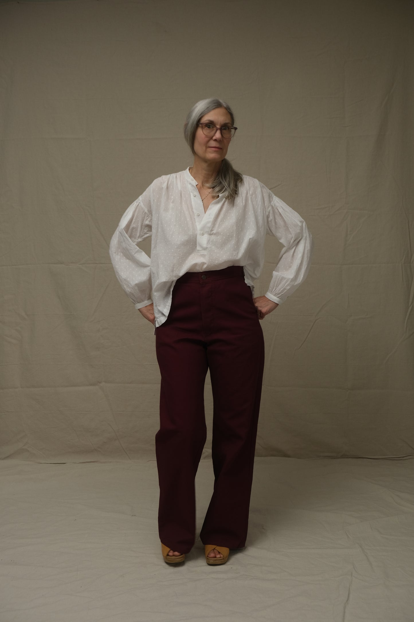 Person wearing a white shirt and maroon pants on a plain background