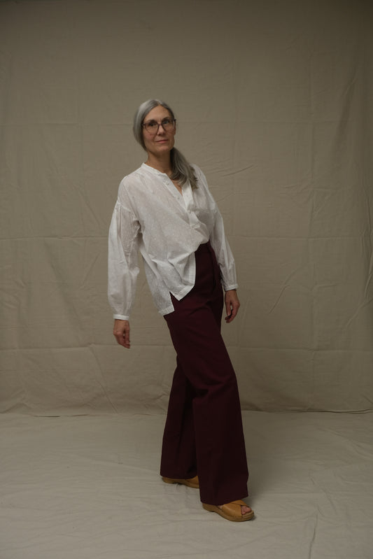 Person wearing a white shirt and maroon pants standing on a plain background