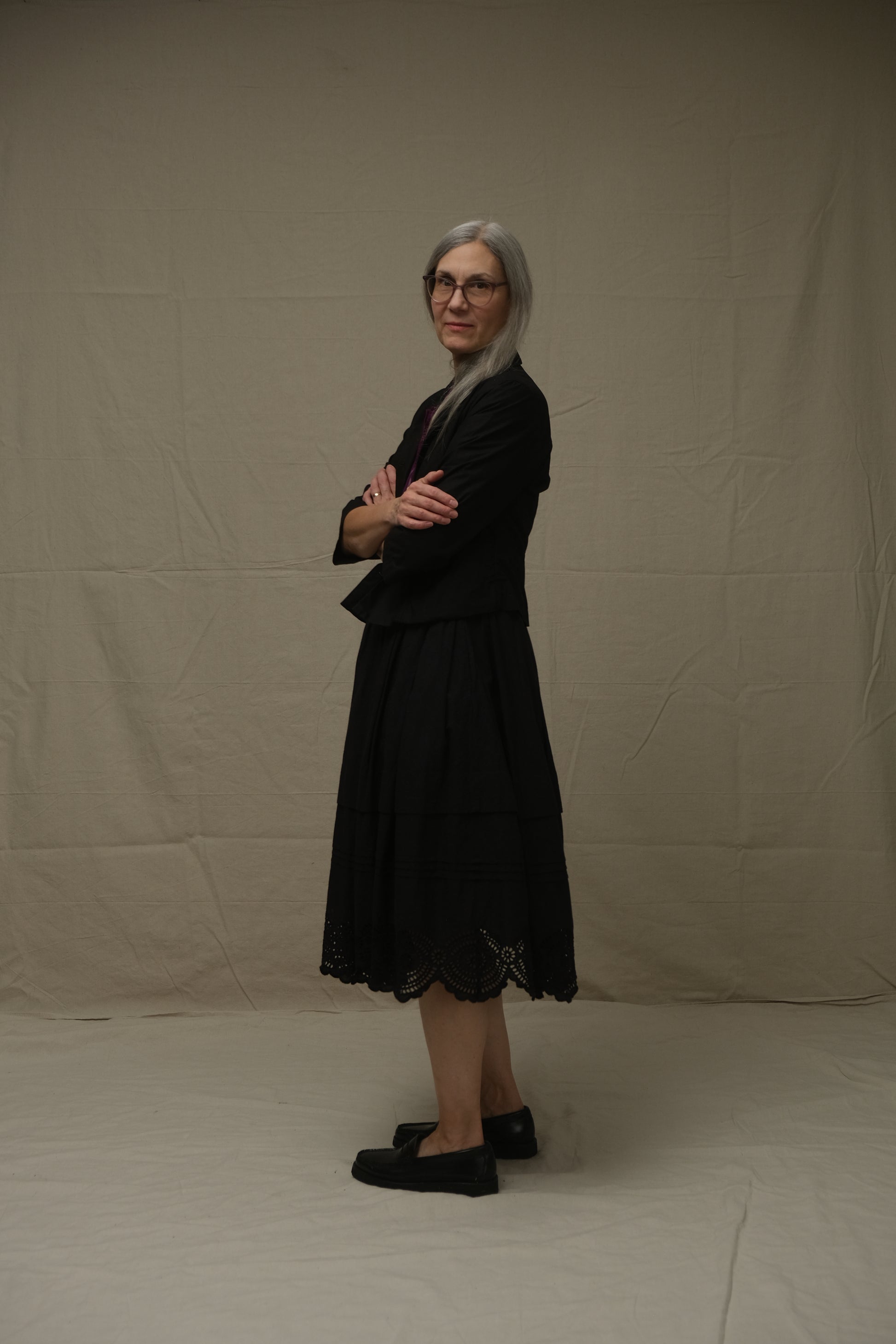 Person wearing a black jacket and skirt standing on a plain background
