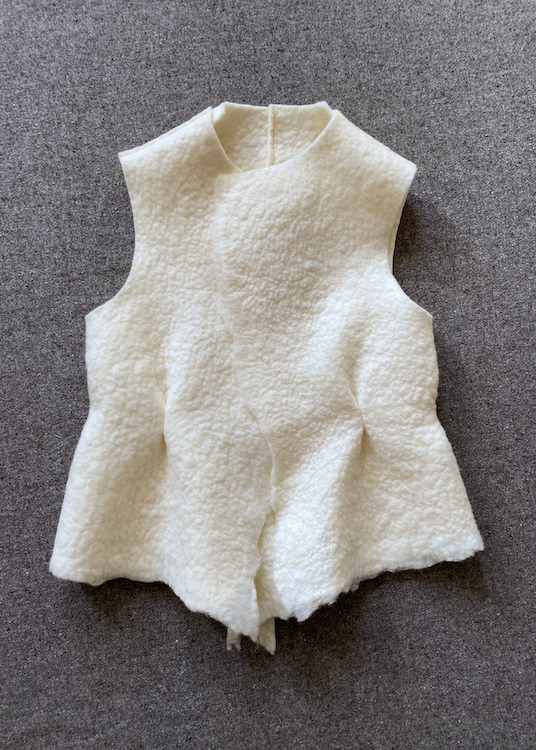 An off-white textured wool vest laid flat on a dark gray fabric background.