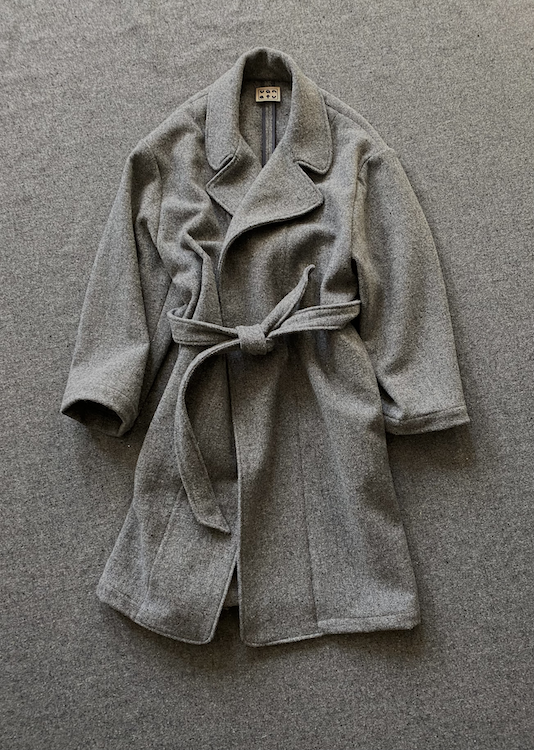 A gray wool-like belted coat or robe laid flat on a textured gray background.