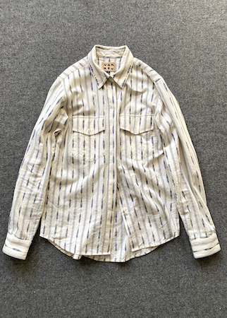A long-sleeve button-up shirt with vertical blue stripes on a cream/off-white base, laid flat on a textured gray surface.